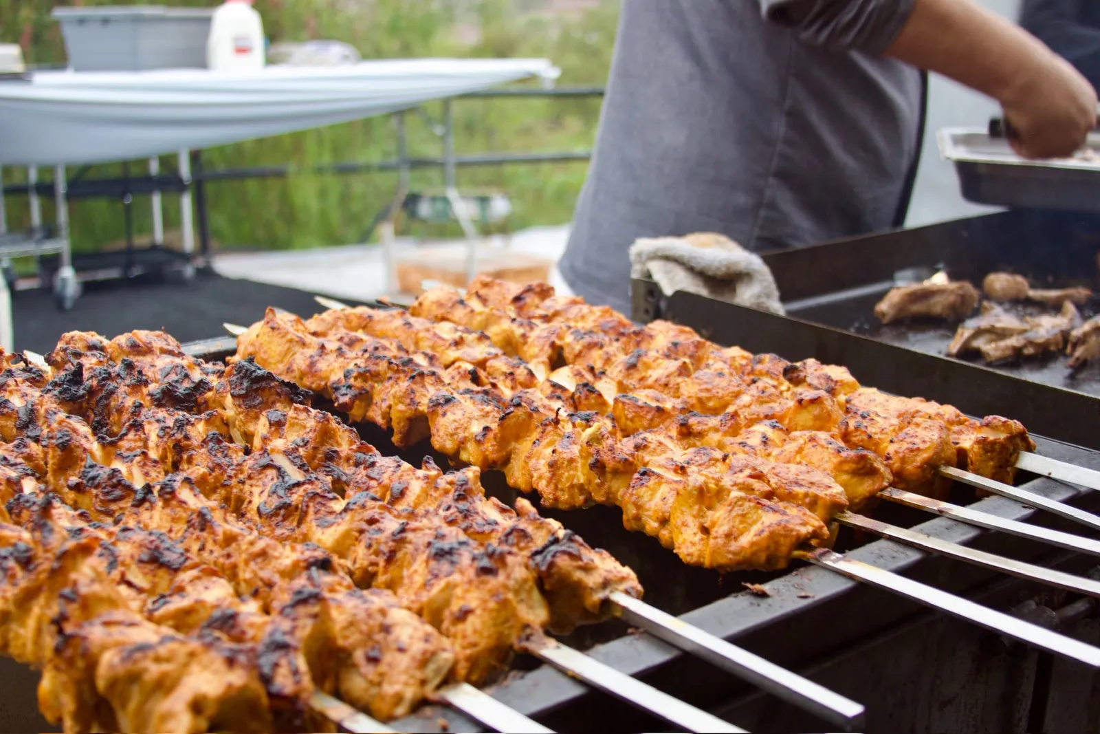 Rows of chicken tikka skewers cooking over a charcoal grill at an outdoor event