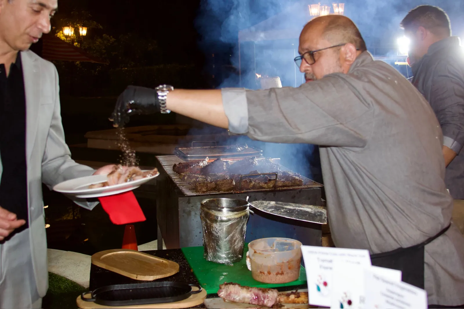 Rasoi Catering chef seasoning charcoal grilled meat at a live grill station during an evening event